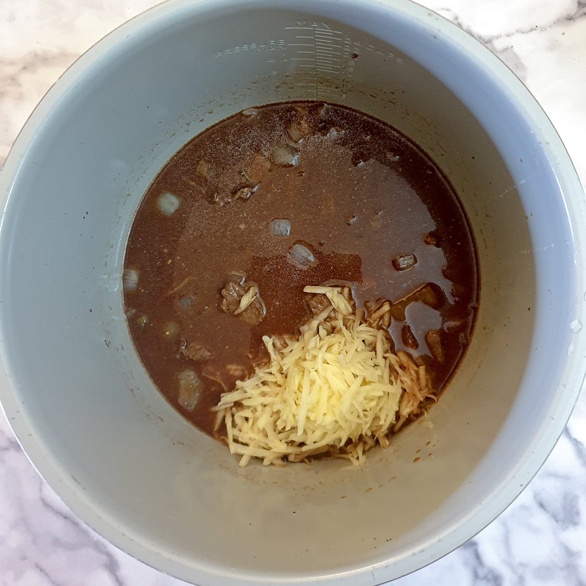 Stock and grated potato added to meat and onions in a pressure cooker.
