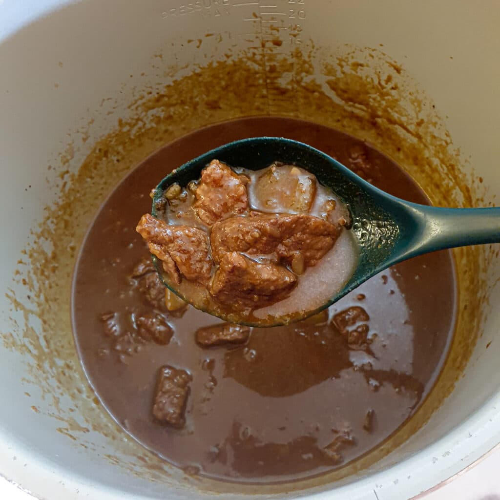 A spoonful of meat and gravy held over a pressure cooker to show the texture of the meat.