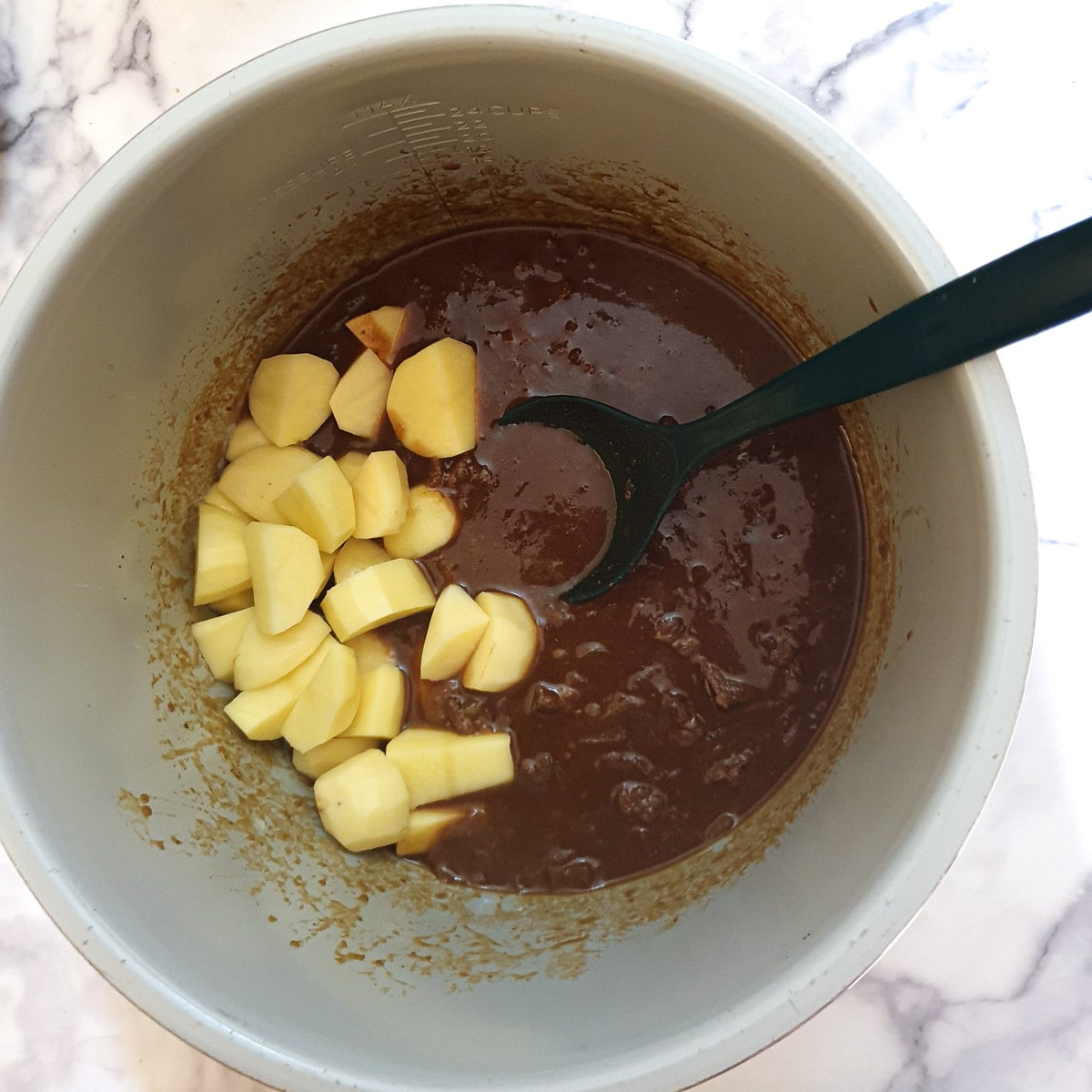 Cubed potatoes being added to the pie filling in a pressure cooker.