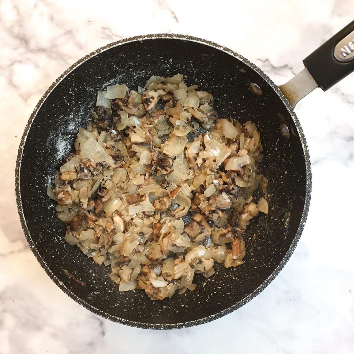 Flour mixed with onions and mushrooms in a frying pan.