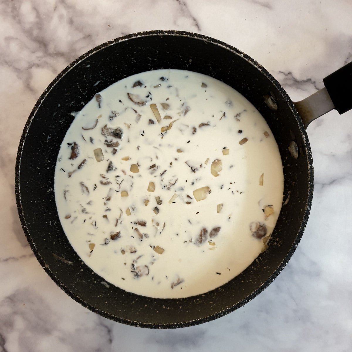 Milk and cream poured into mushrooms and onions in a frying pan.