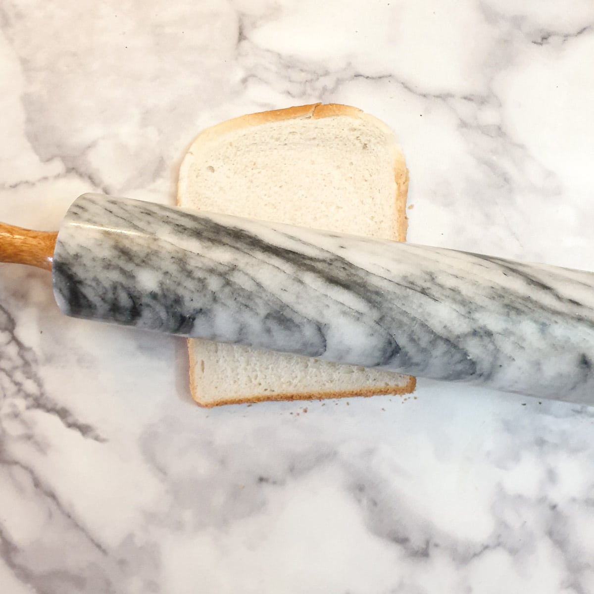 A rolling pin flattening a slice of white bread.