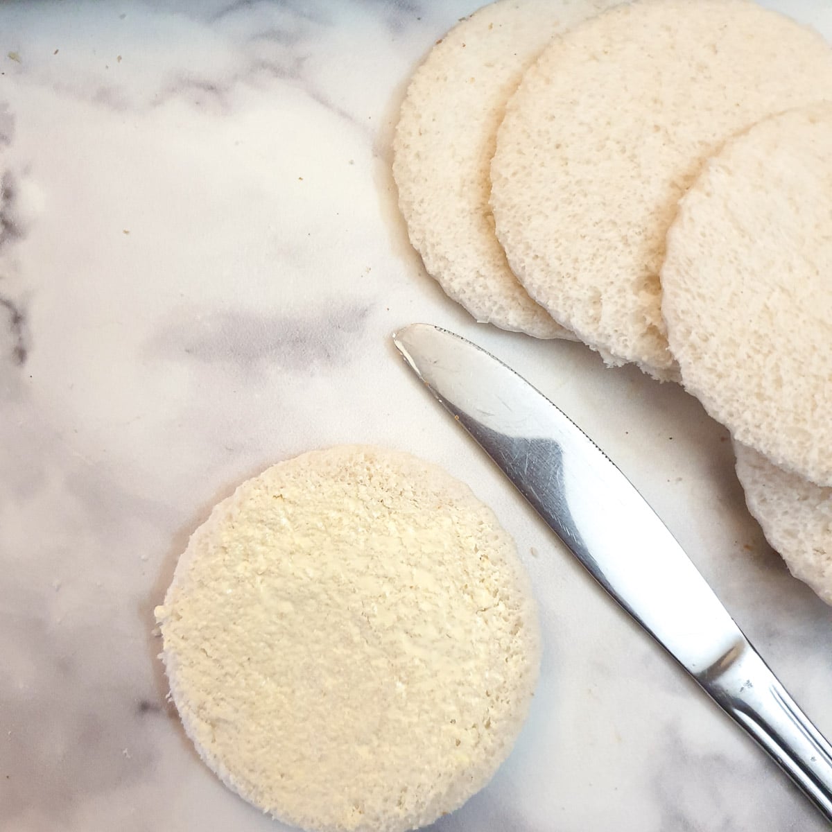 Rounds of bread being spread with butter.