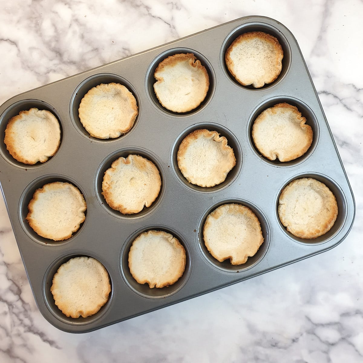 A 12-hole muffin pan with 12 toasted rounds of bread.