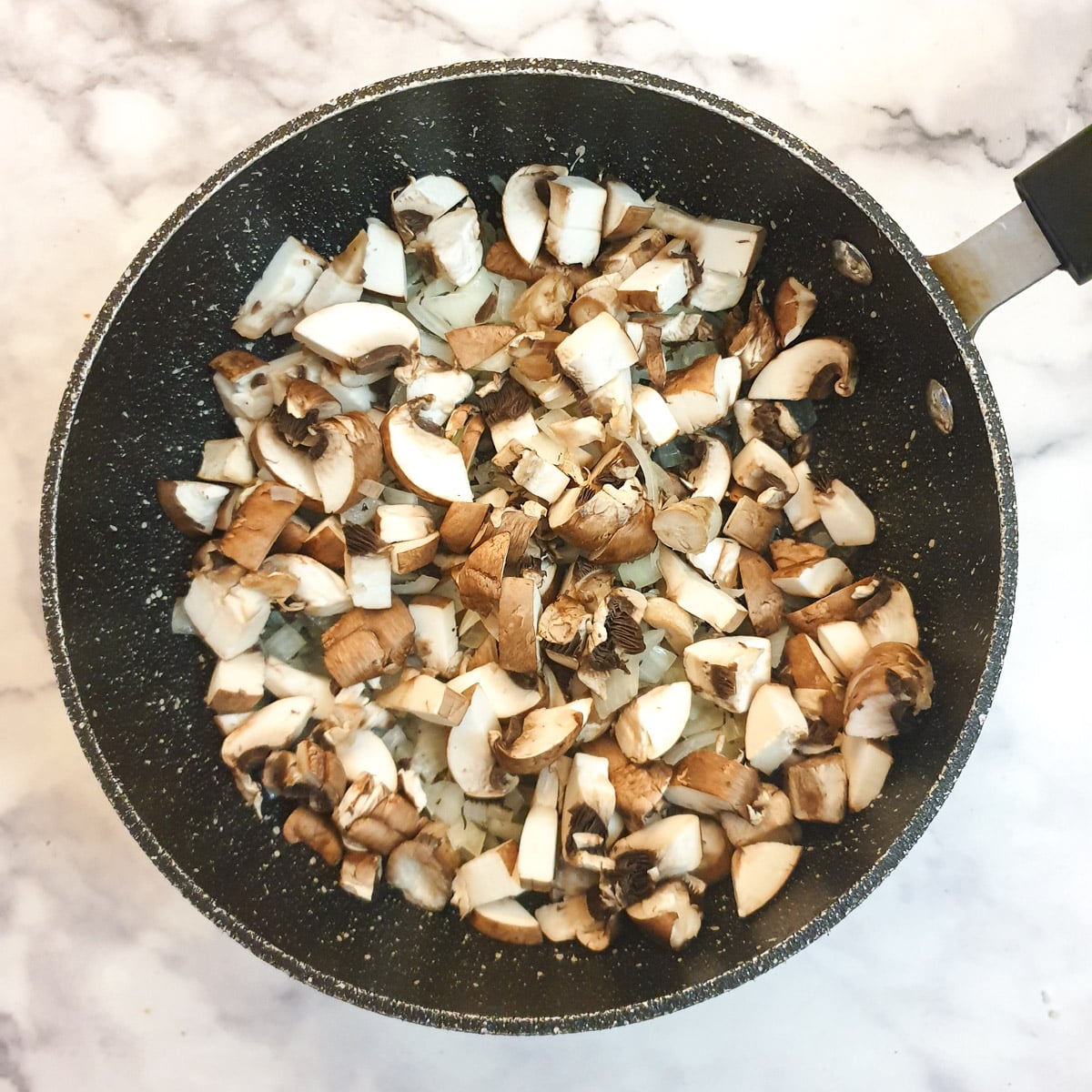 Chopped mushrooms added to onions in a frying pan.
