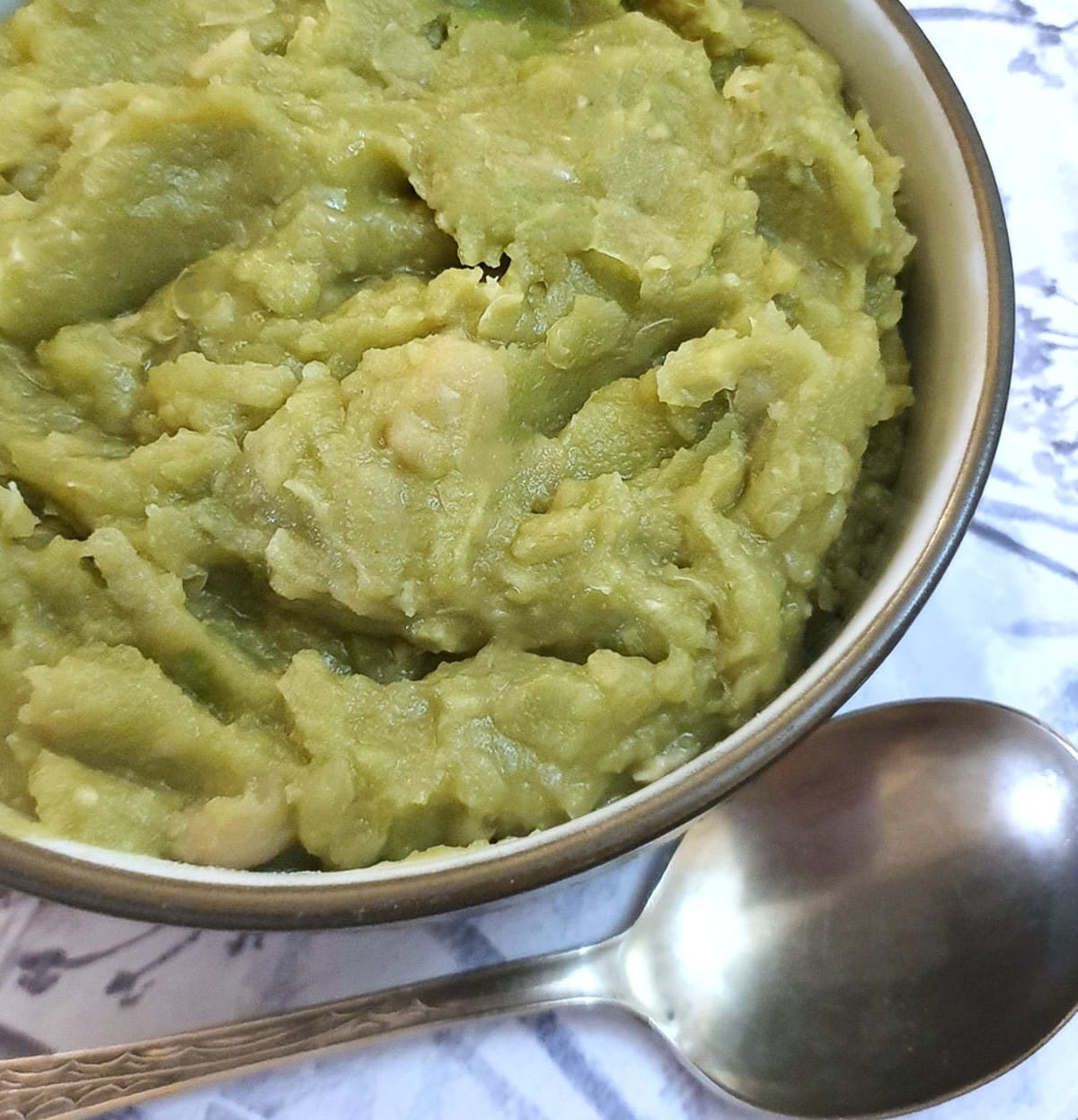 Close up of mushy peas in a bowl next to a spoon.