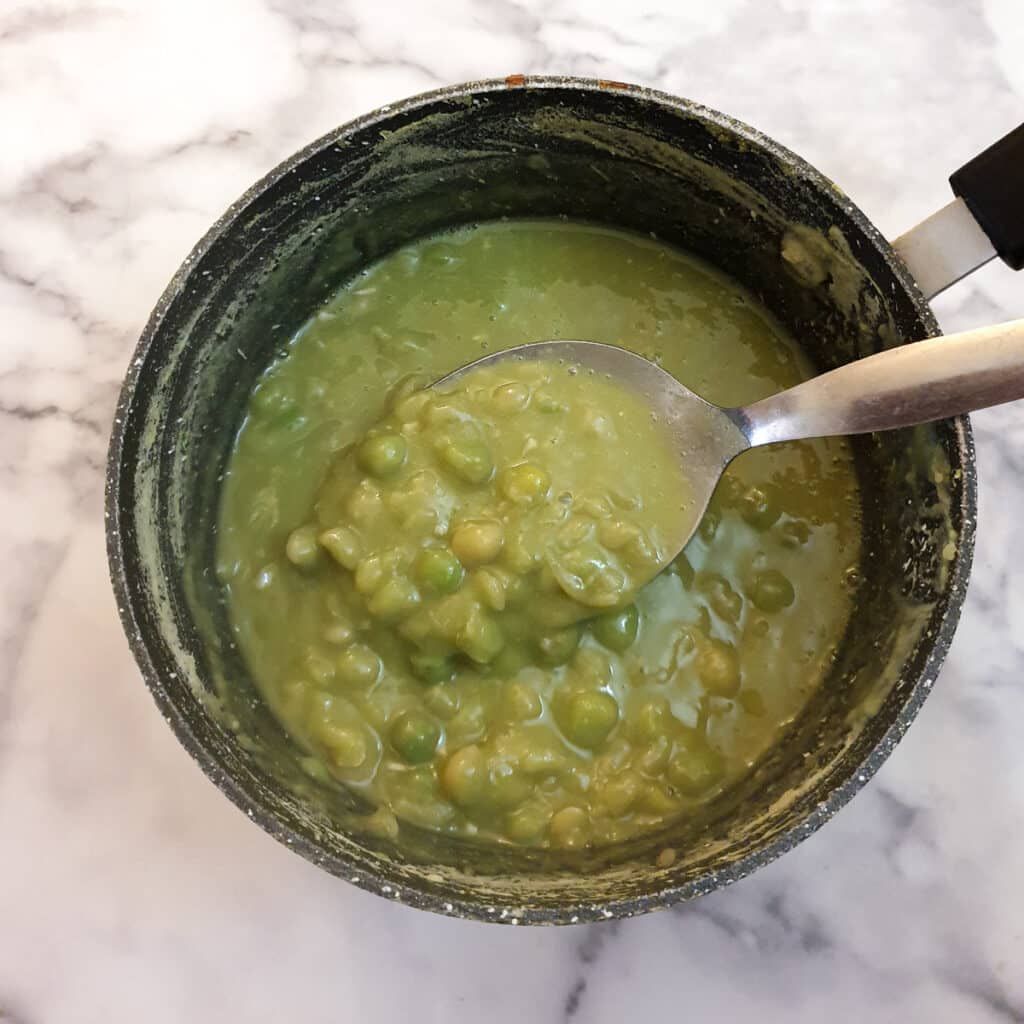 Cooked mushy peas in a pan with a spoon.