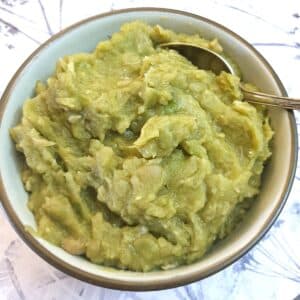 A bowl of mushy peas in a dish with a spoon.