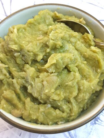 A bowl of mushy peas in a dish with a spoon.