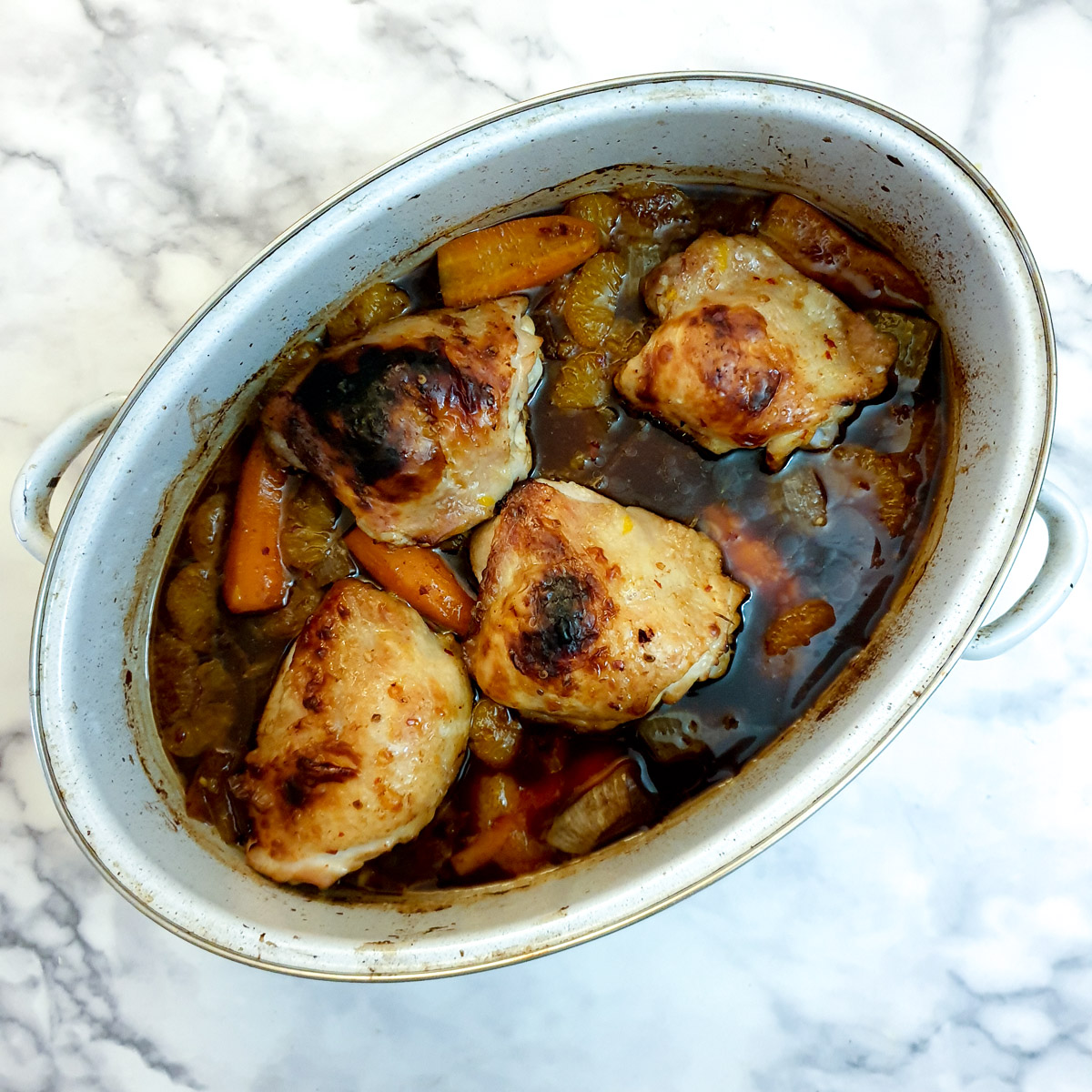 4 browned chicken thighs with gravy in a light blue roasting pan.