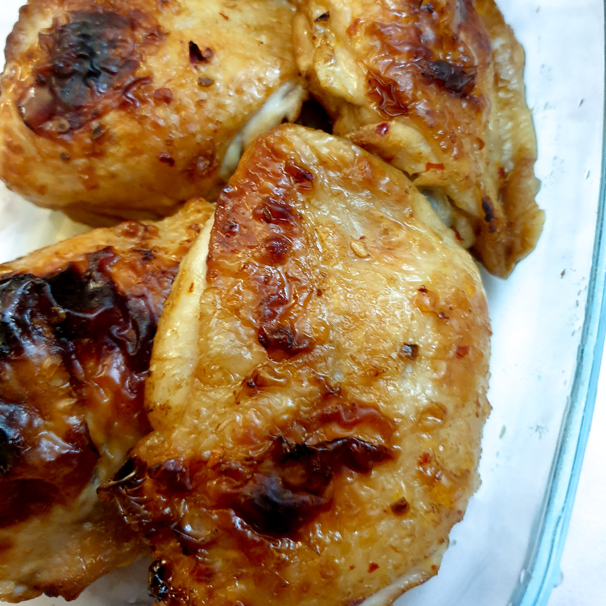 Close up of 4 browned chicken thighs in a glass serving dish.