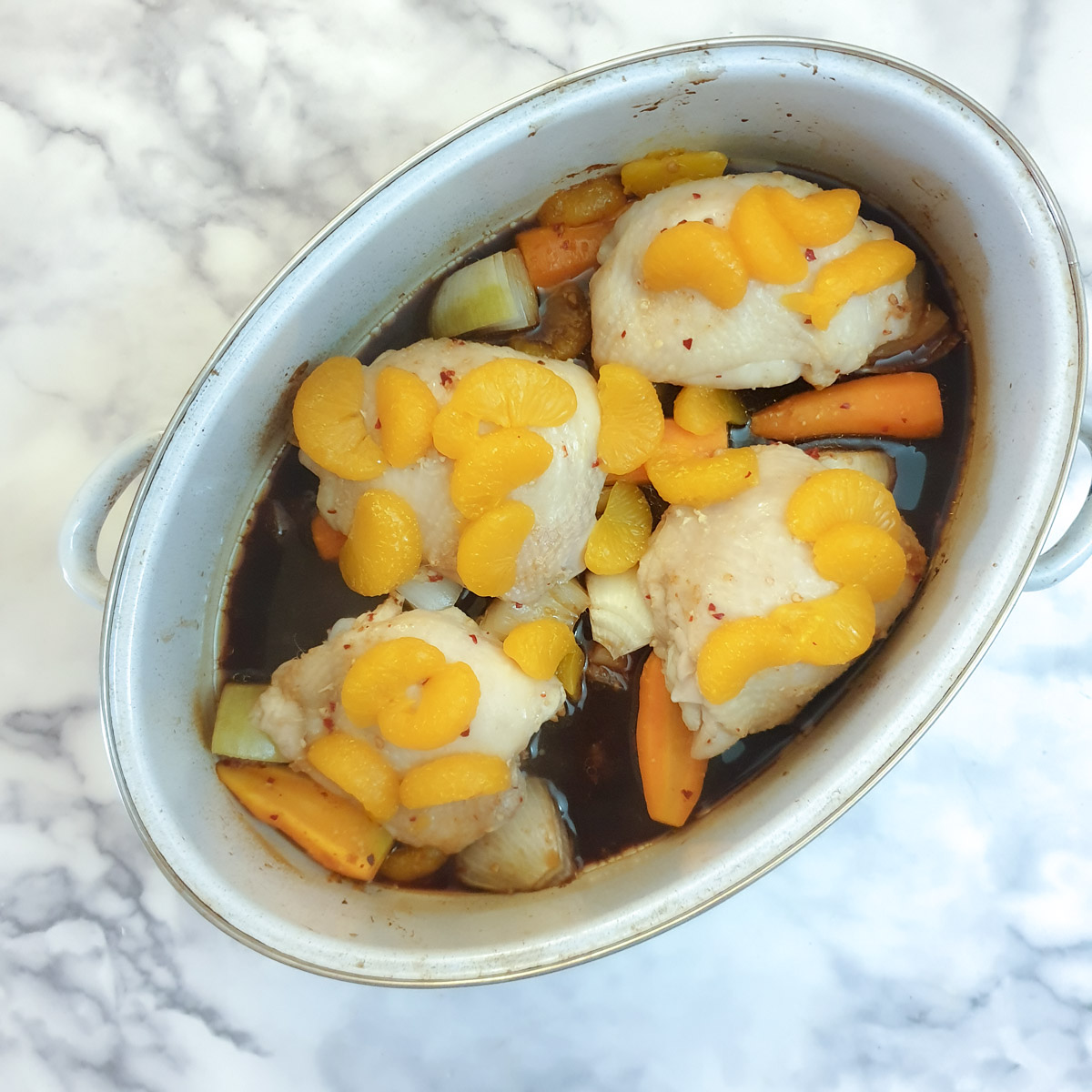 4 cooked chicken thighs covered with orange segments and gravy in a light blue roasting pan.