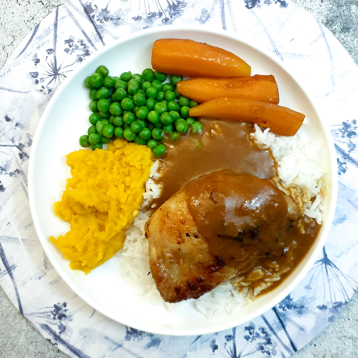 Overhead shot of a plate of chicken thighs on a bed of rice with vegetables and gravy.