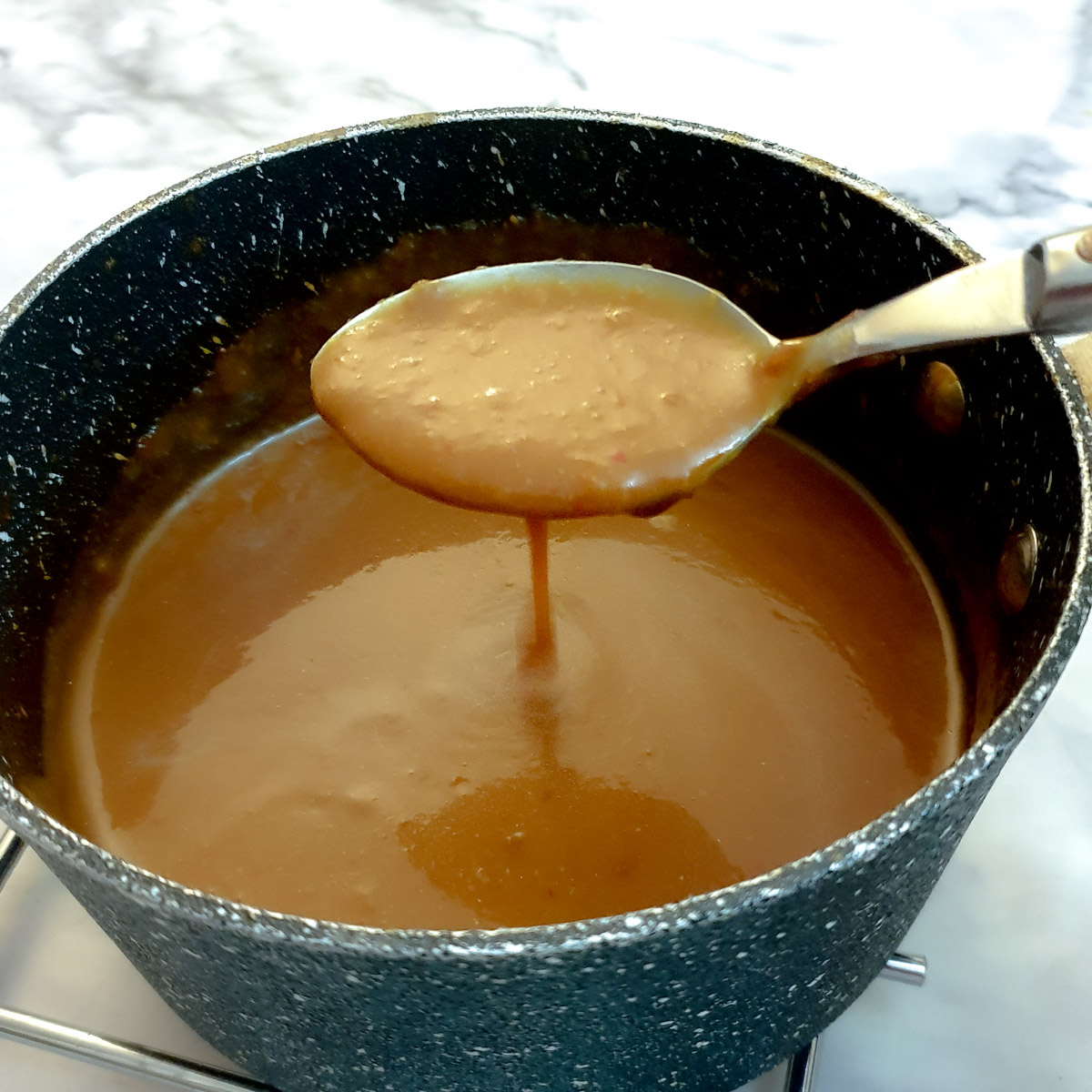 A spoonful of thickened gravy held over a saucepan.