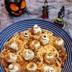 A blue and white striped serving dish filled with spaghetti in tomato sauce and topped with halloween eyeball meatballs.