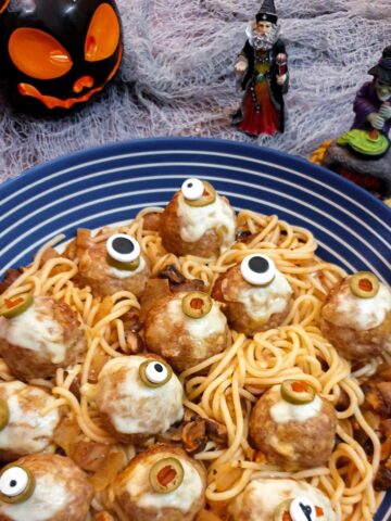 A blue and white striped serving dish filled with spaghetti in tomato sauce and topped with halloween eyeball meatballs.