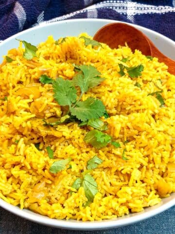 A white serving dish holding yellow pilau rice and a wooden serving spoon.