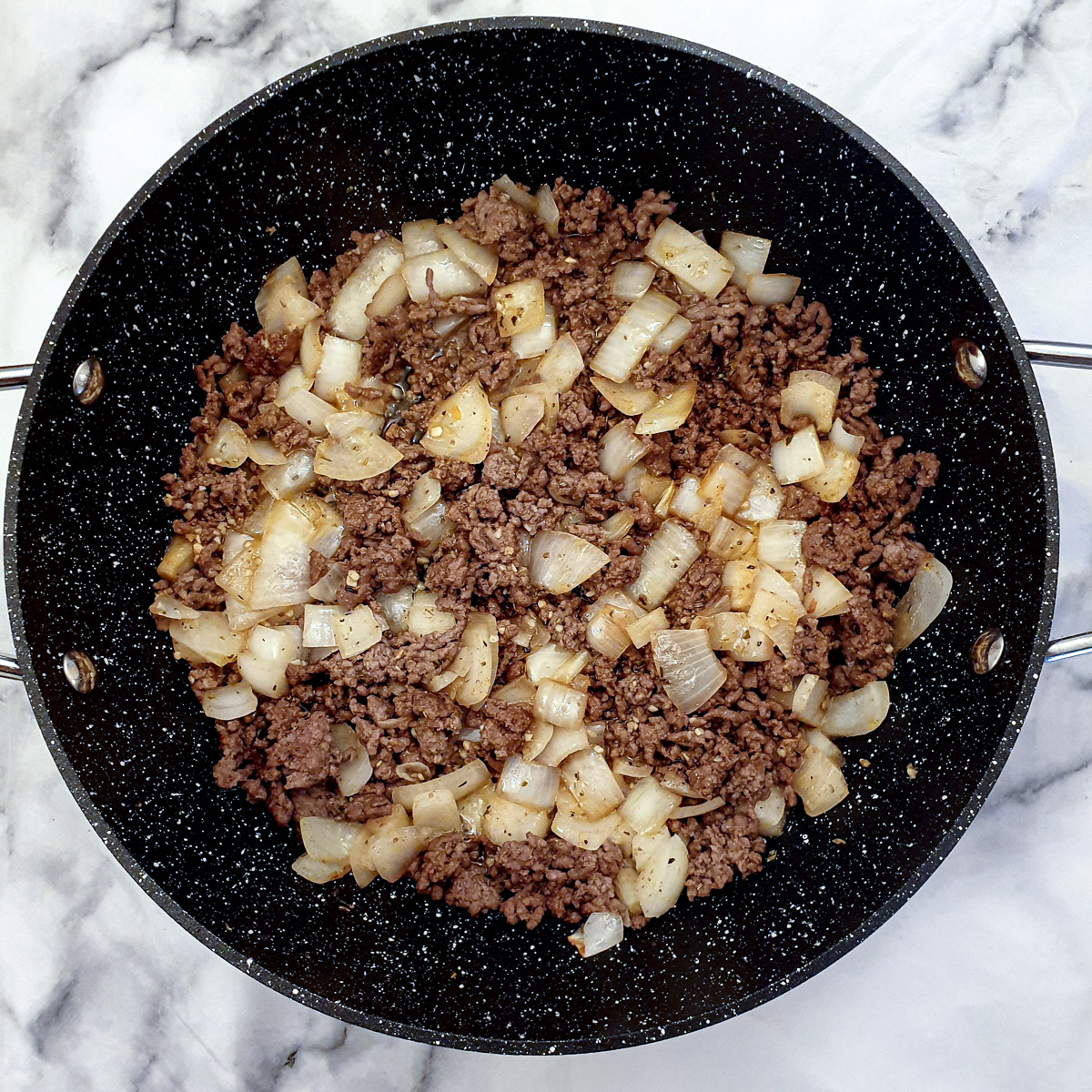 Chopped onions and par-cooked ground beef in a black frying pan.