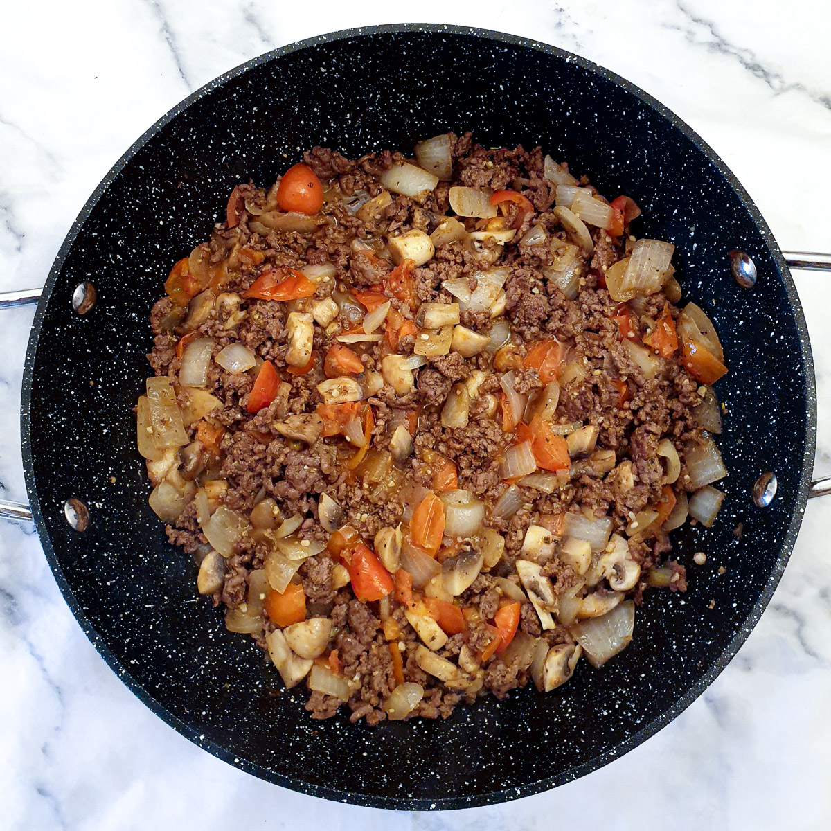 Chopped tomatoes and mushrooms added to pan of ground beef and onions.