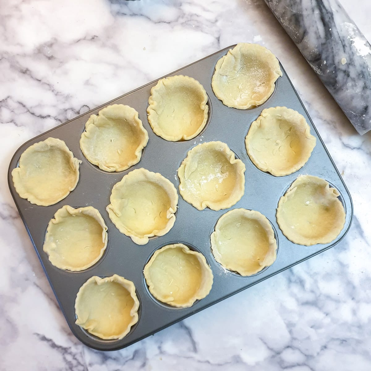 A 12-hole muffin tin lined with 12 circles of pastry.