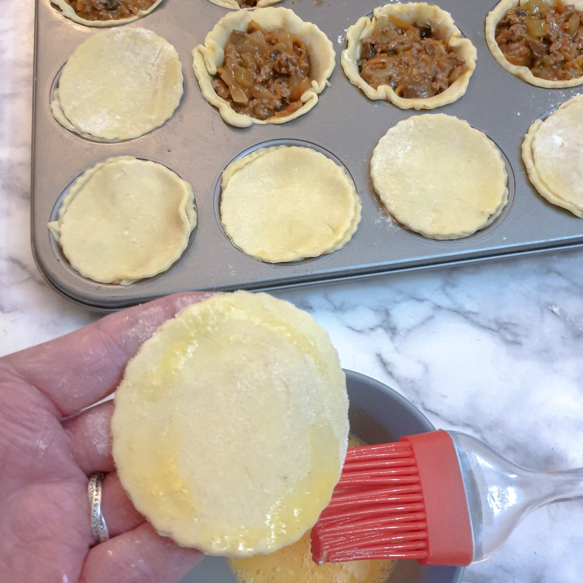 Close up of a pastry lid being brushed with beaten egg.