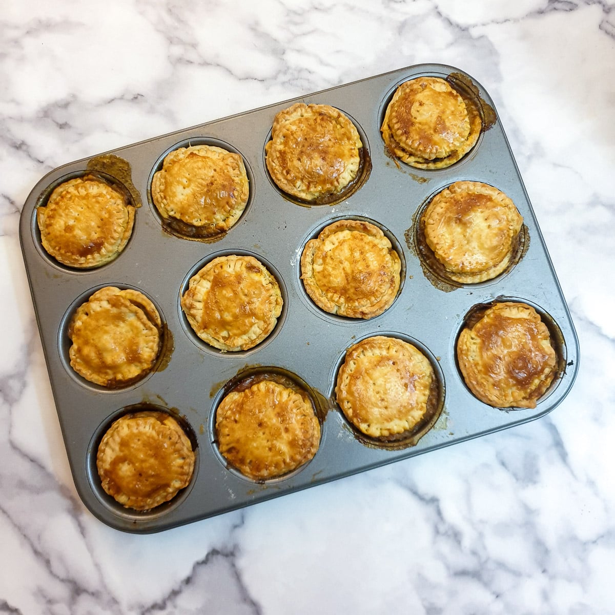 12 baked beef and onion pies in a muffin tin.