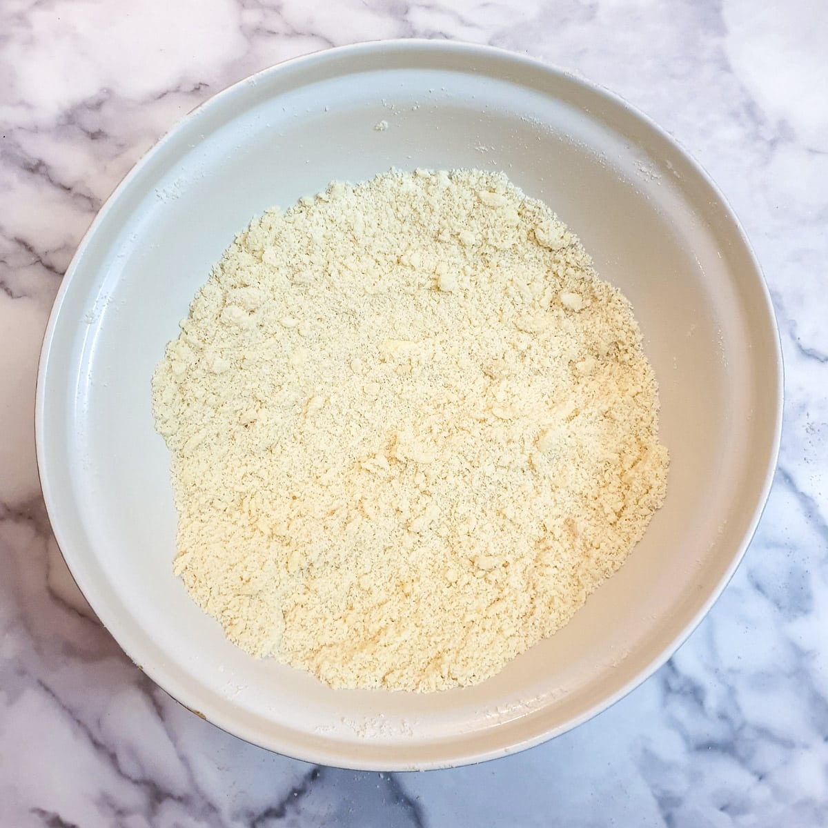 Flour and butter rubbed together to form fine breadcrumbs in a large white mixing bowl.