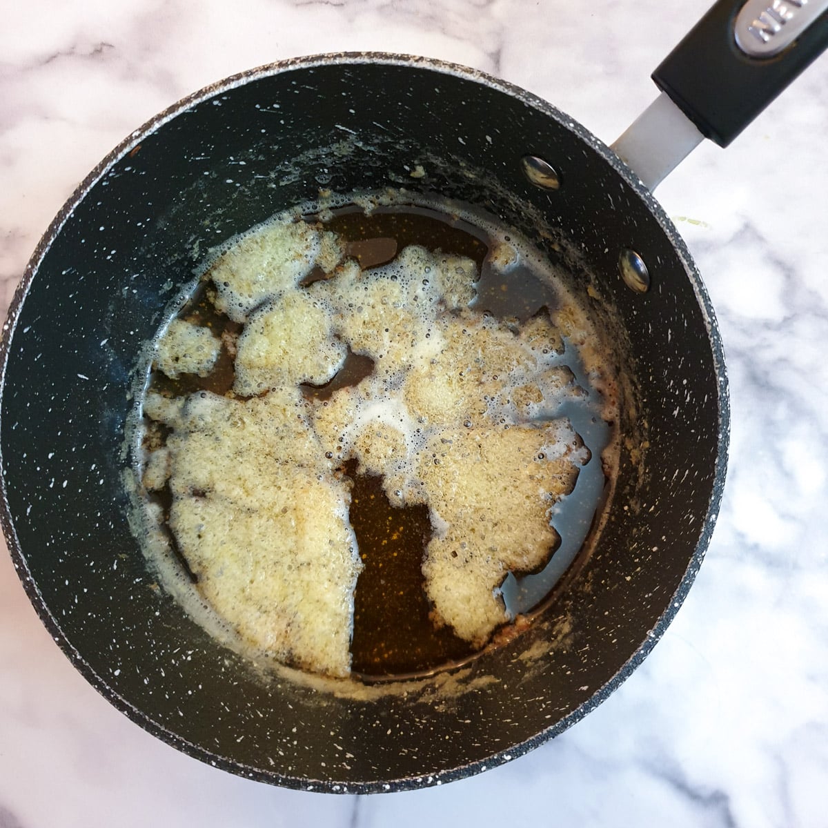 Separated milk solids floating of top of melted butter in a saucepan.