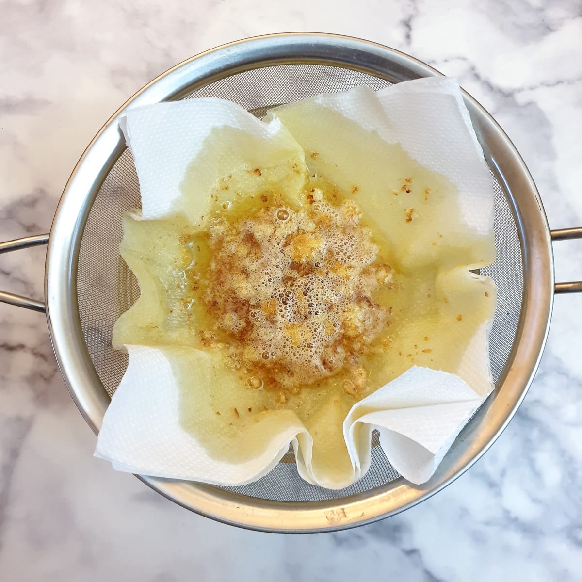 Liquid ghee being strained through a sieve lined with paper towel.