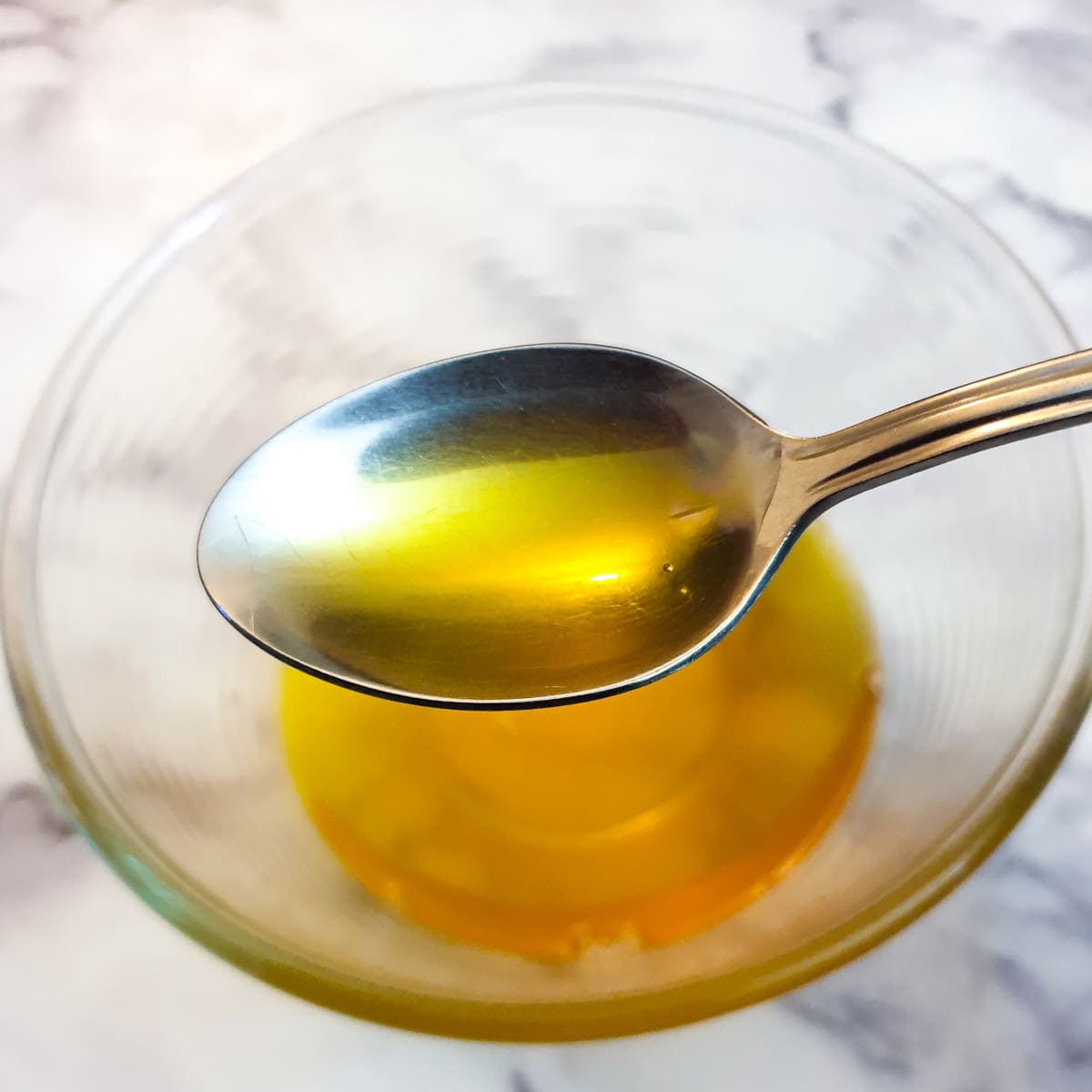 A spoonful of liquid ghee held over a glass bowl.