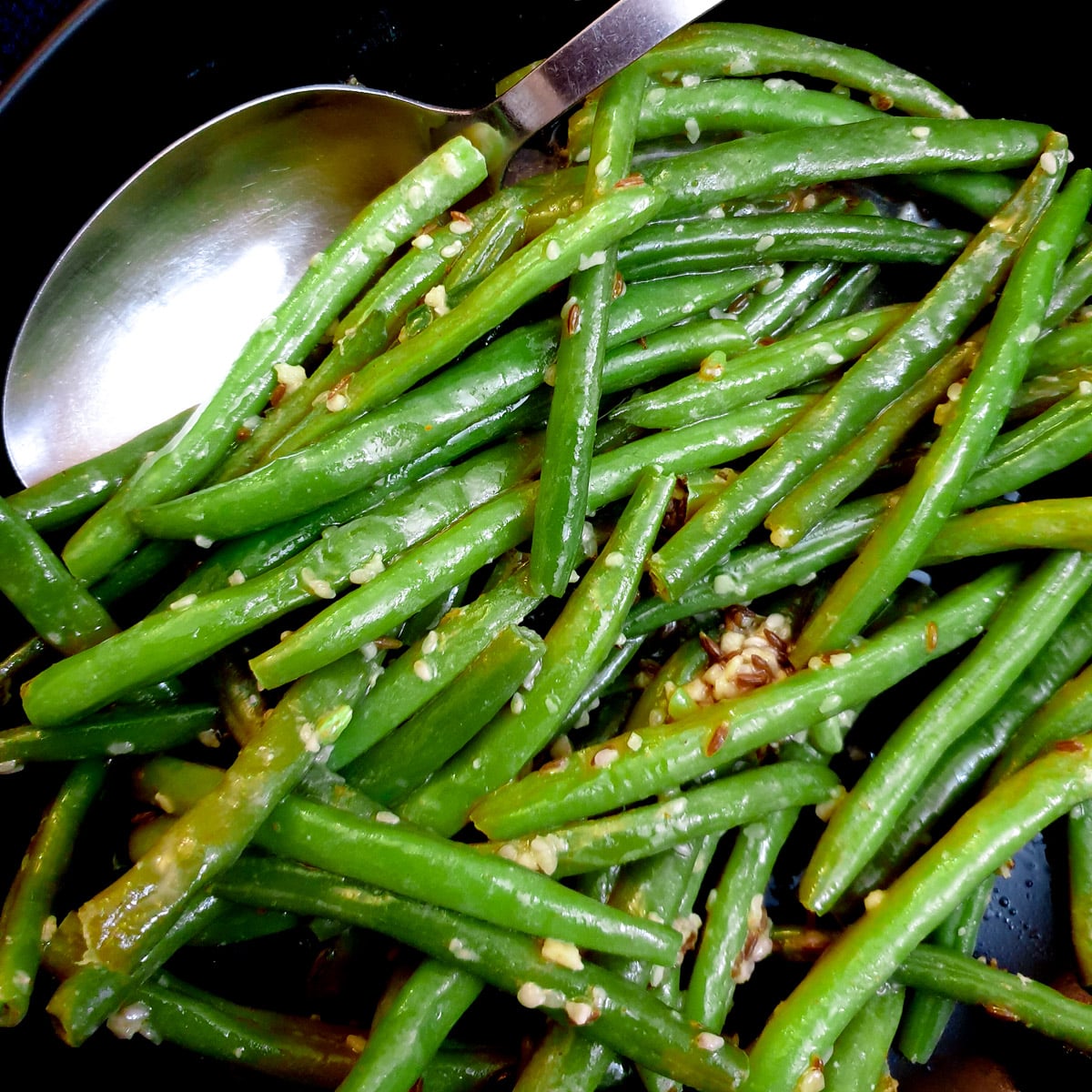 Close up of Indian-style green beans in a black dish with a serving spoon.