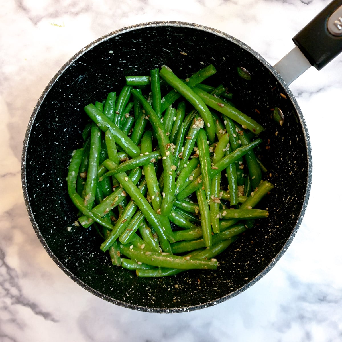 Indian-style green beans in a saucepan, mixed with the fried spices.