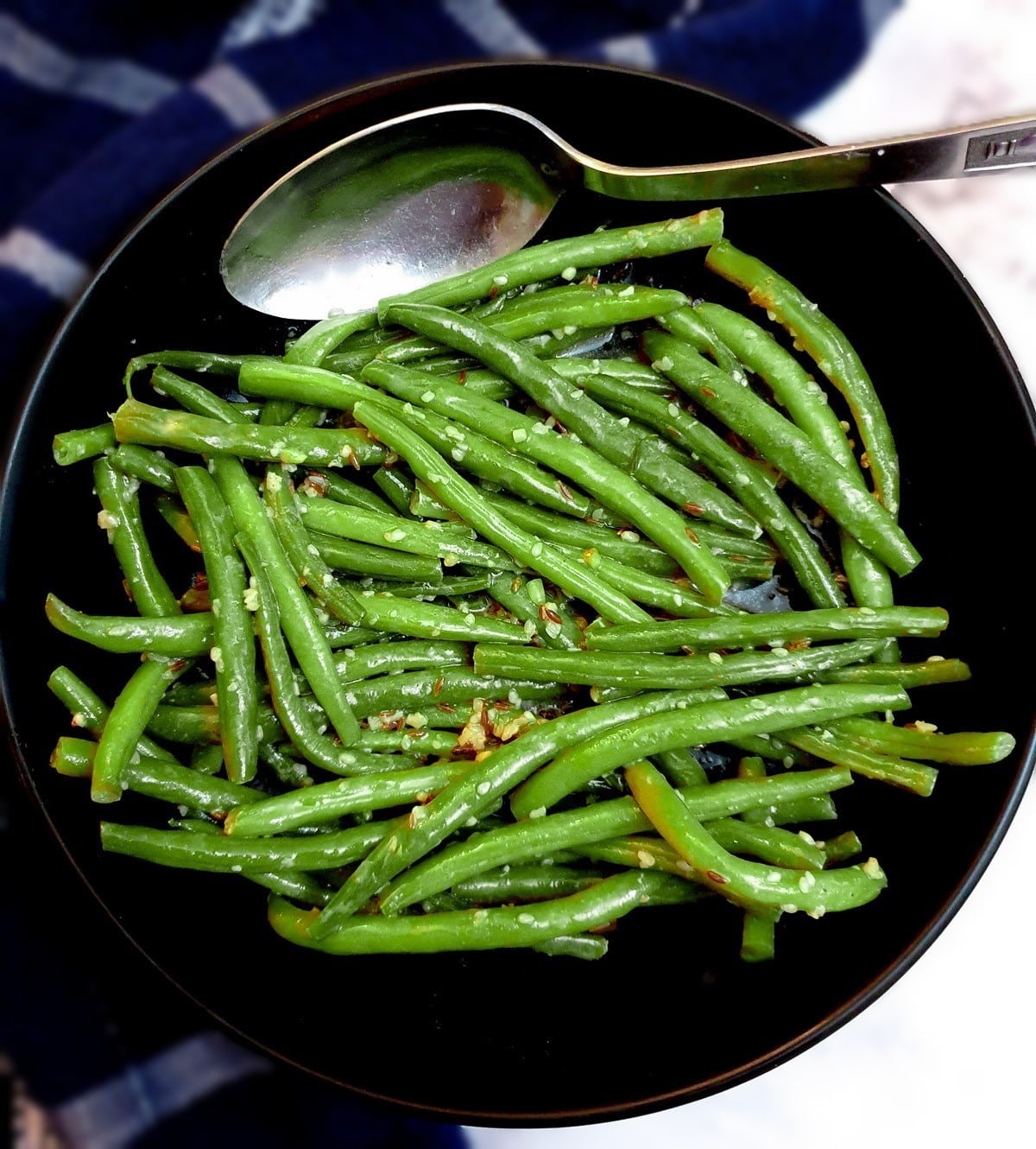 A black serving dish of Indian-style green beans with a serving spoon.