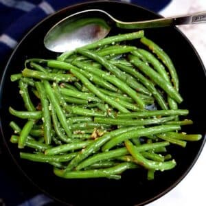 A black serving dish of Indian-style green beans with a serving spoon.