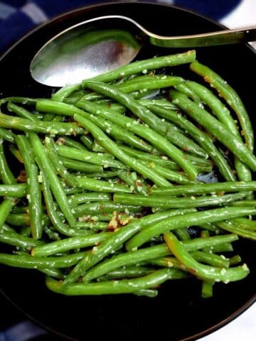 A black serving dish of Indian-style green beans with a serving spoon.