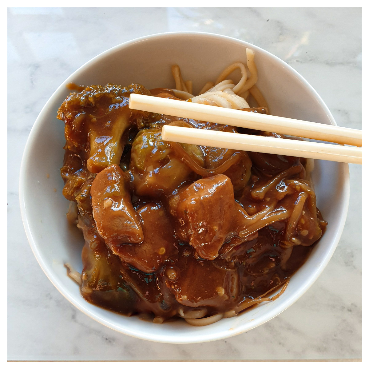 Roast pork in garlic sauce in a white bowl with a pair of chopsticks.