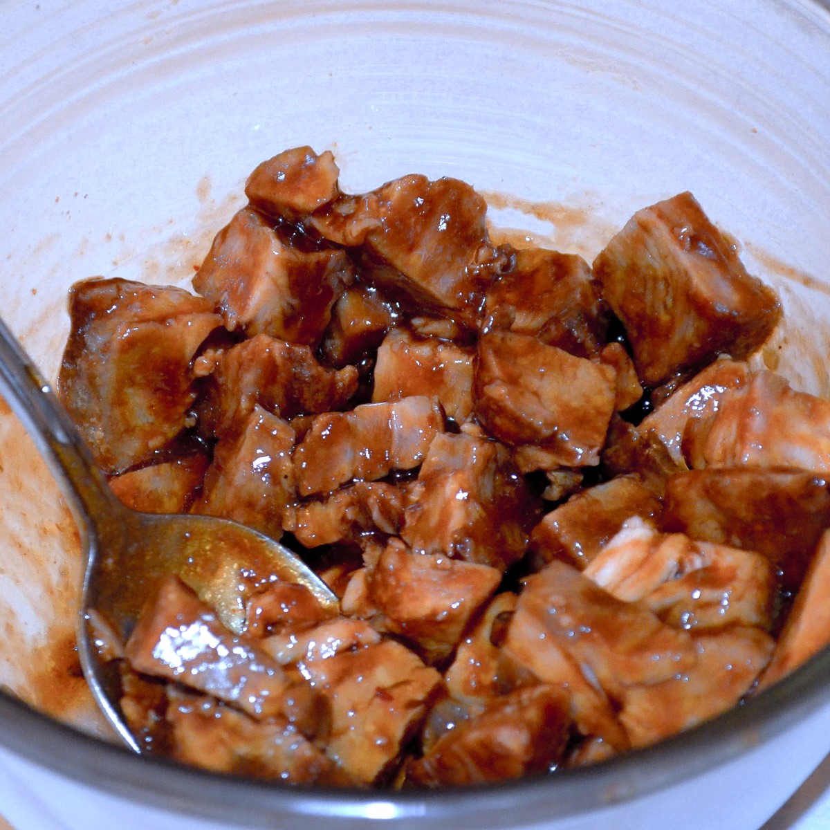 Cubed cooked roast pork marinating in a glass bowl.
