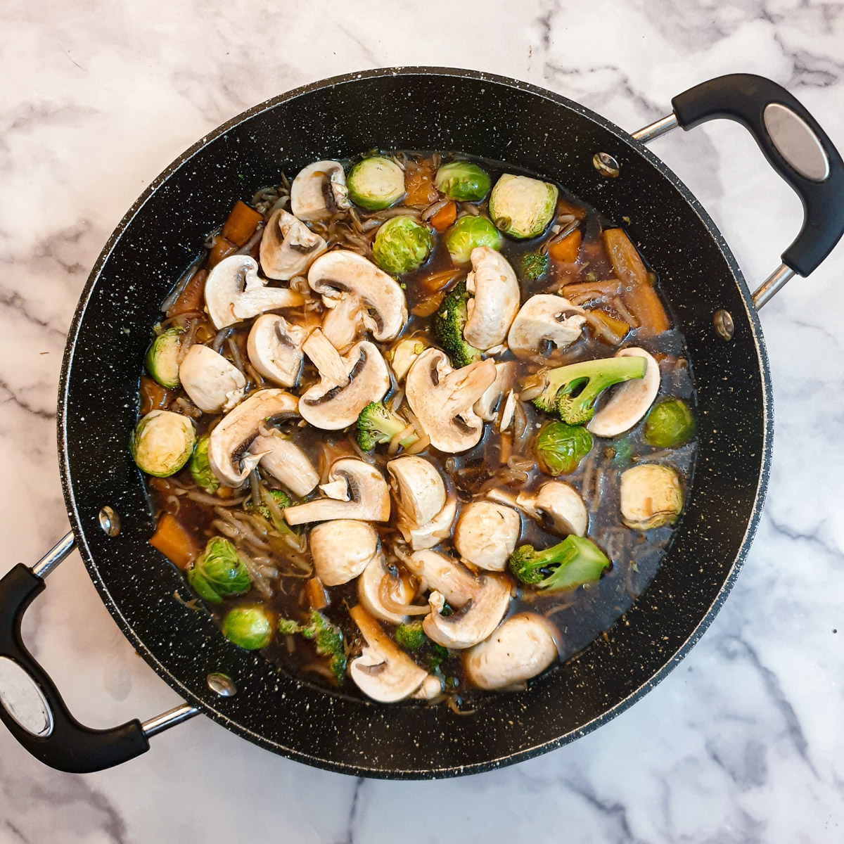 Sliced mushrooms on top of vegtables and garlic sauce in a frying pan.