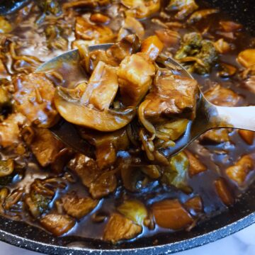 A spoonful of leftover pork in garlic sauce held over a frying pan.