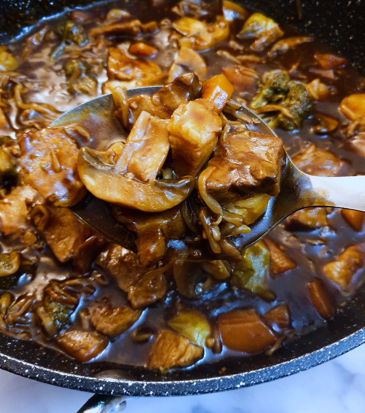 A spoonful of leftover pork in garlic sauce held over a frying pan.