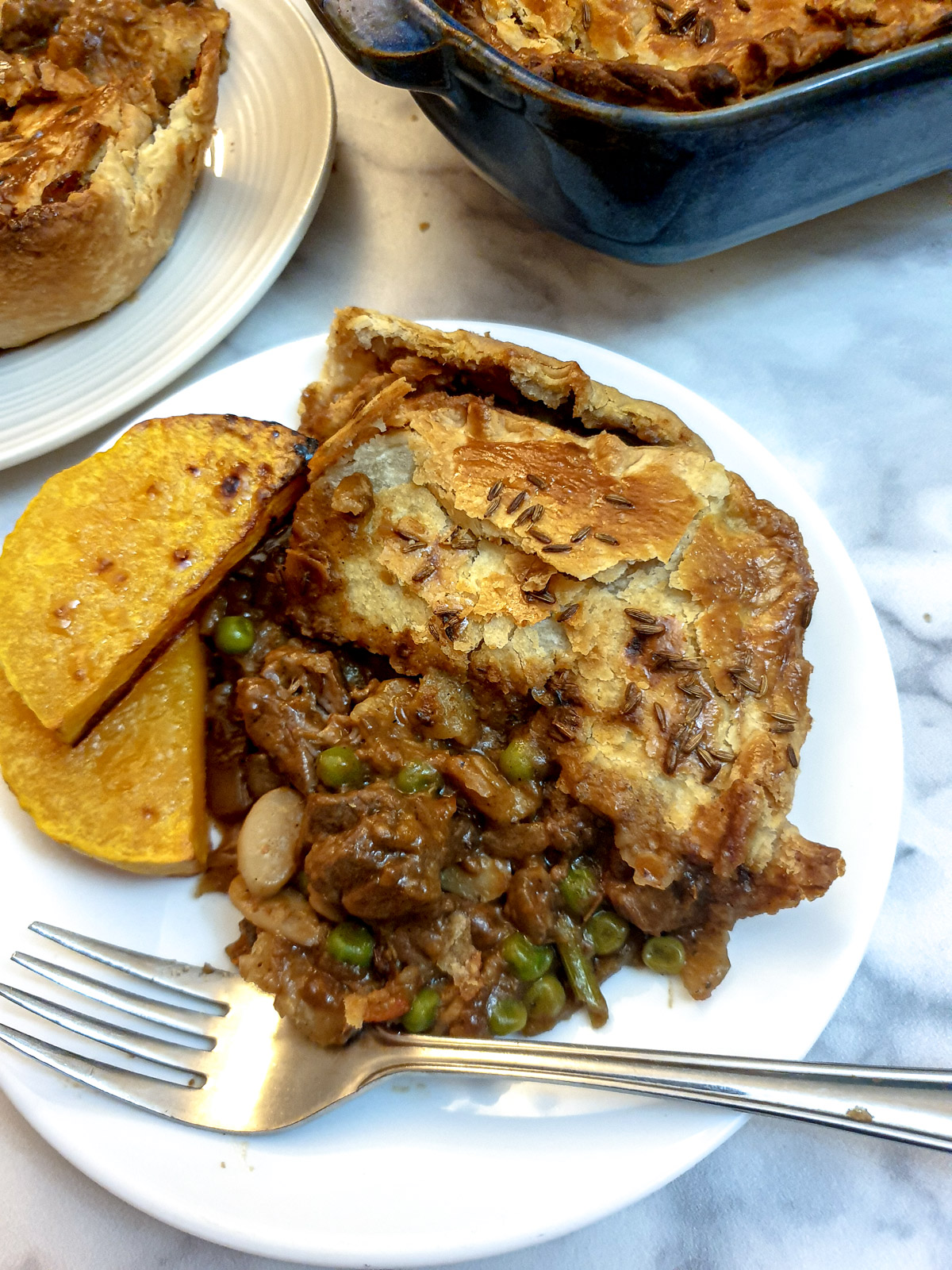 A slice of Moroccan lamb pie on a white plate with two slices of roasted butternut squash.