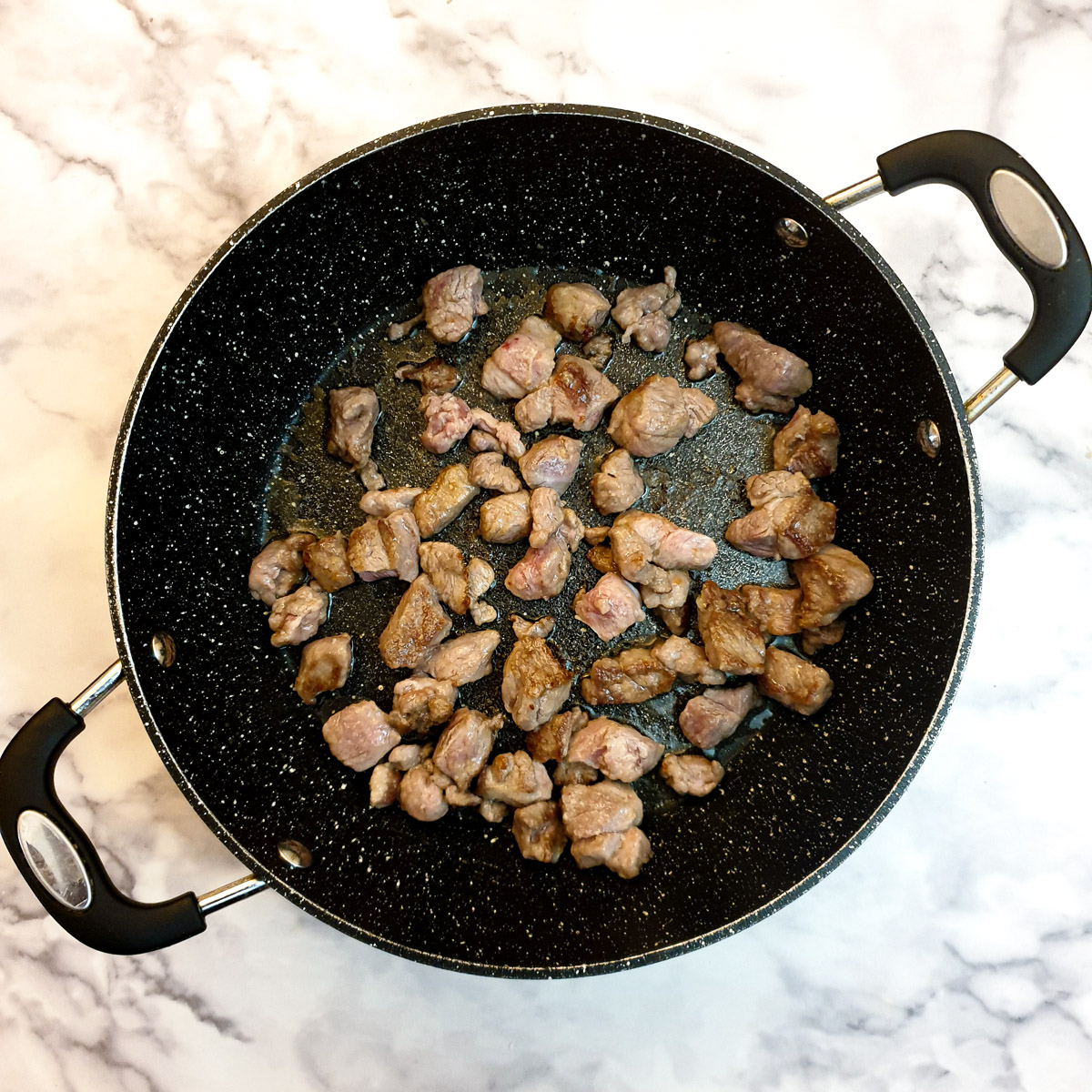 Lamb cubes browning in a frying pan.