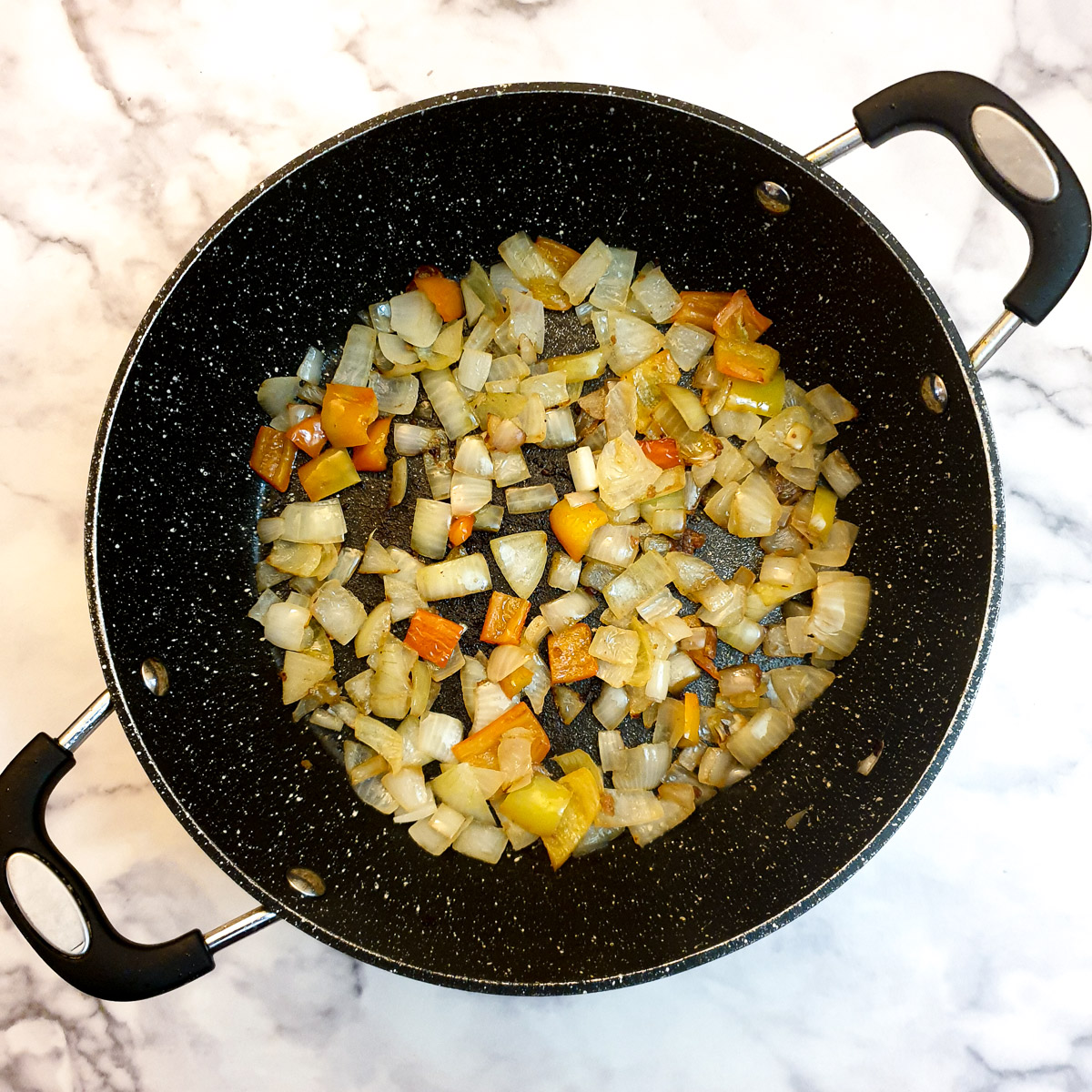 Onions and red pepper frying in a frying pan.