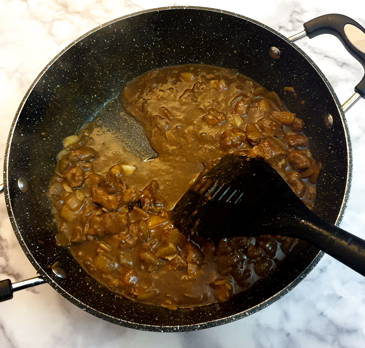 A spatula being drawn through the Moroccan lamb pie filling to show the consistency of the gravy.