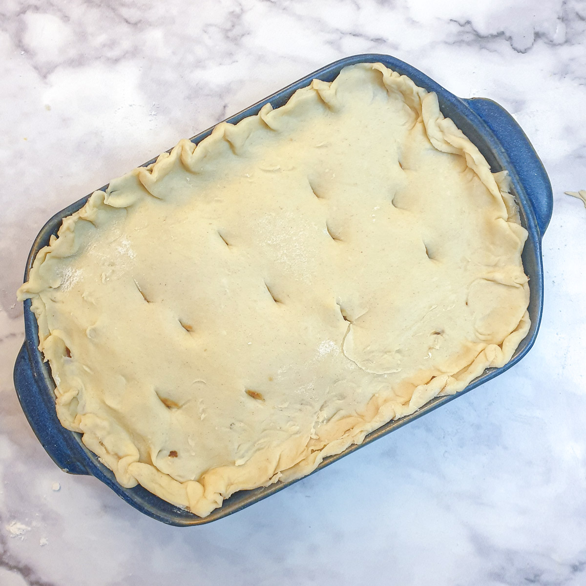 An unbaked Moroccan lamb pie with the pastry lid added, in a blue baking dish.