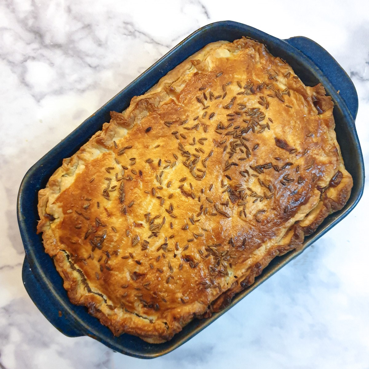 Overhead shot of a baked Moroccan lamb pie in a blue dish.
