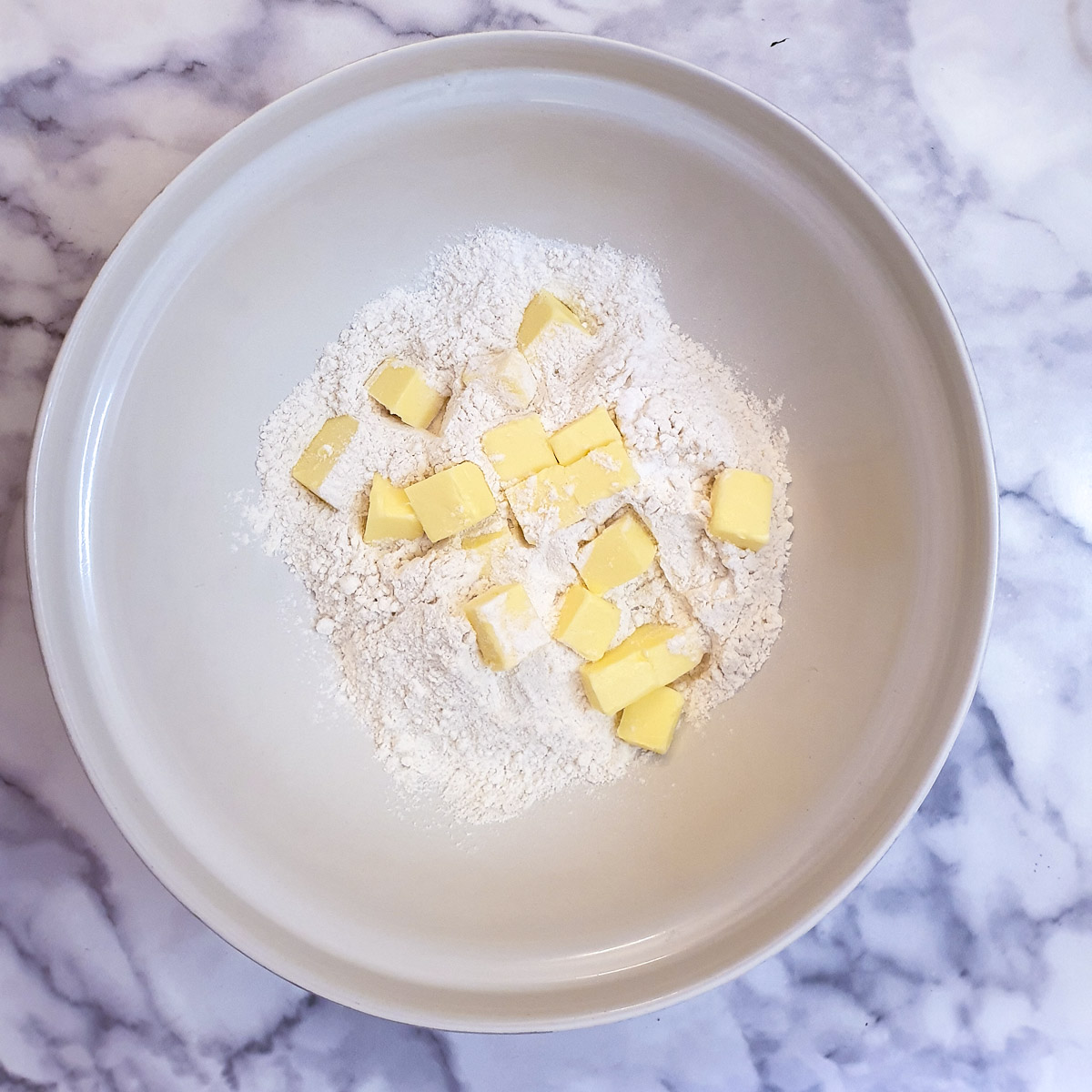 Cubed butter and flour in a large white mixing bowl.