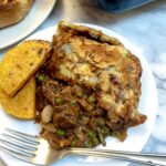 A slice of Moroccan lamb pie on a white plate with two slices of roasted butternut squash.