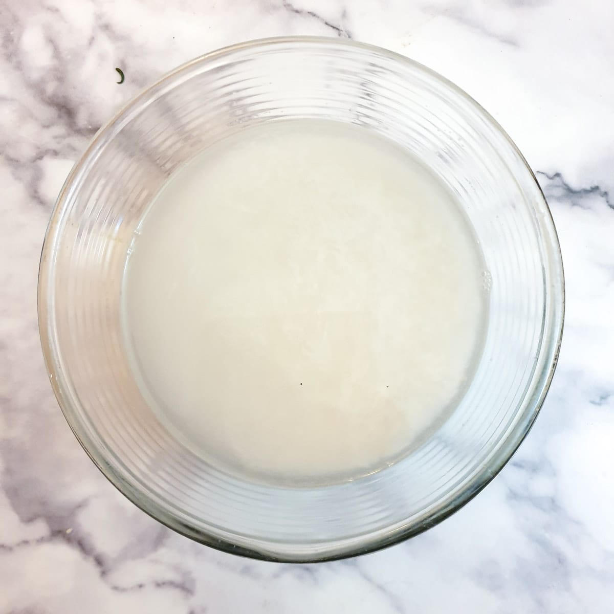 A glass bowl of rice in water showing how cloudy the water gets a the starch is rinsed from the rice.