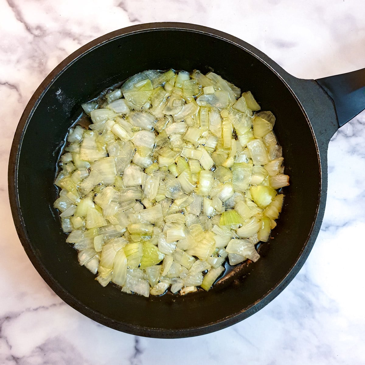 Chopped onions frying in ghee in a black frying pan.